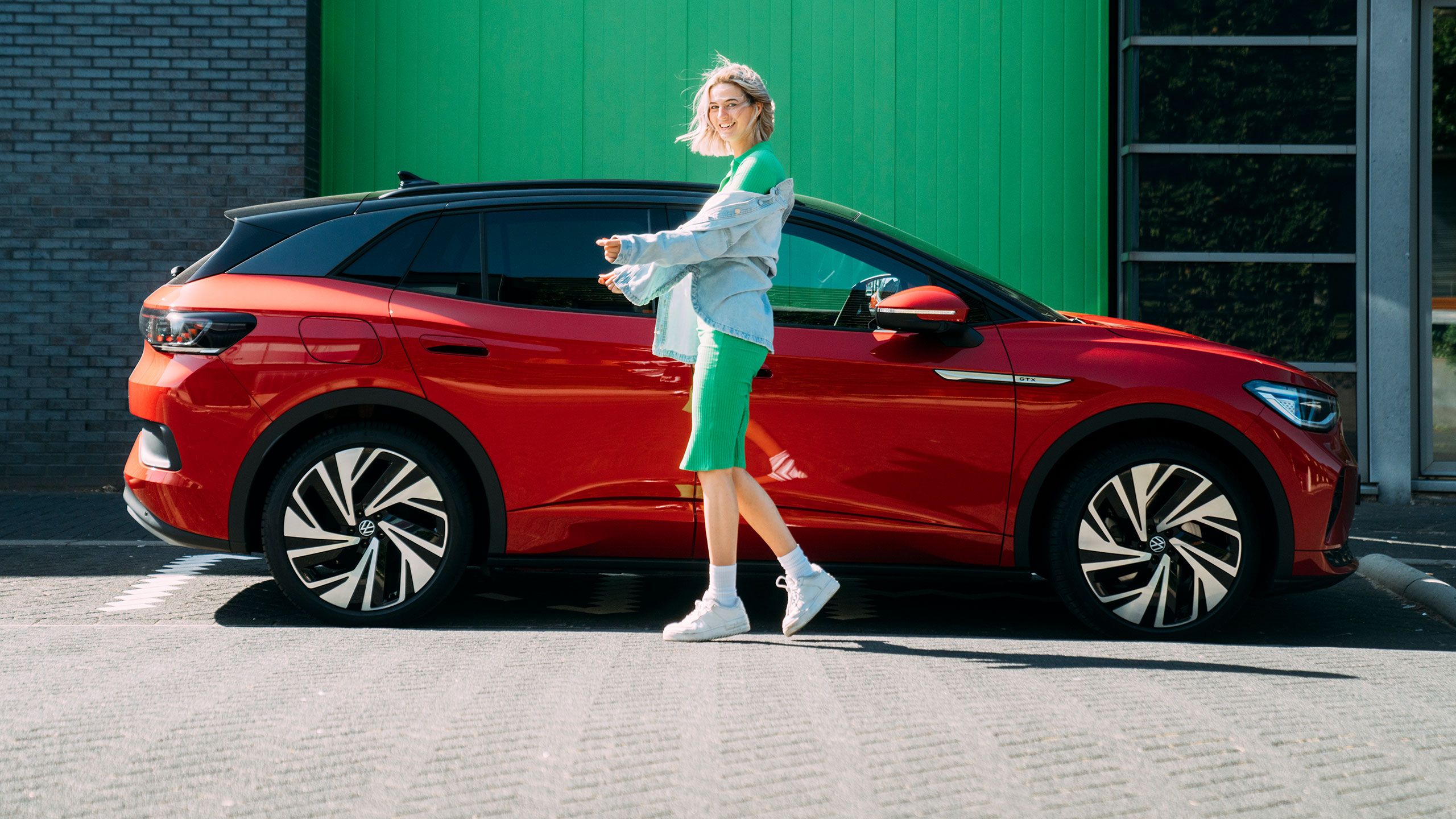 Eine Frau steht vor ihrem parkenden VW ID. Modell in Rot