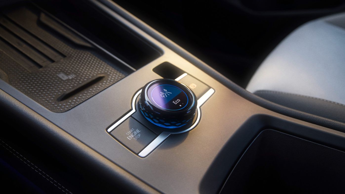 Nahaufnahme einer Mittelkonsole in einem T-Roc mit Fokus auf den Fahrerlebnisschalter. Ein runder Drehknopf mit LED-Anzeigen zur Steuerung verschiedener Fahrzeugfunktionen. Hochwertige Materialien und ein elegantes Design sind zu erkennen.