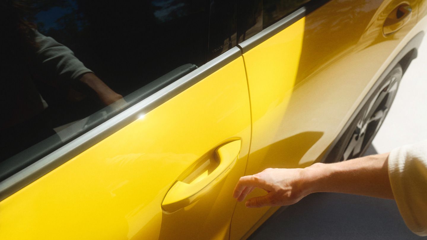 Ein Mensch greift nach dem Türgriff eines gelben Autos. Der Schatten der Hand ist auf dem hellen Boden zu sehen. Das Auto steht still.