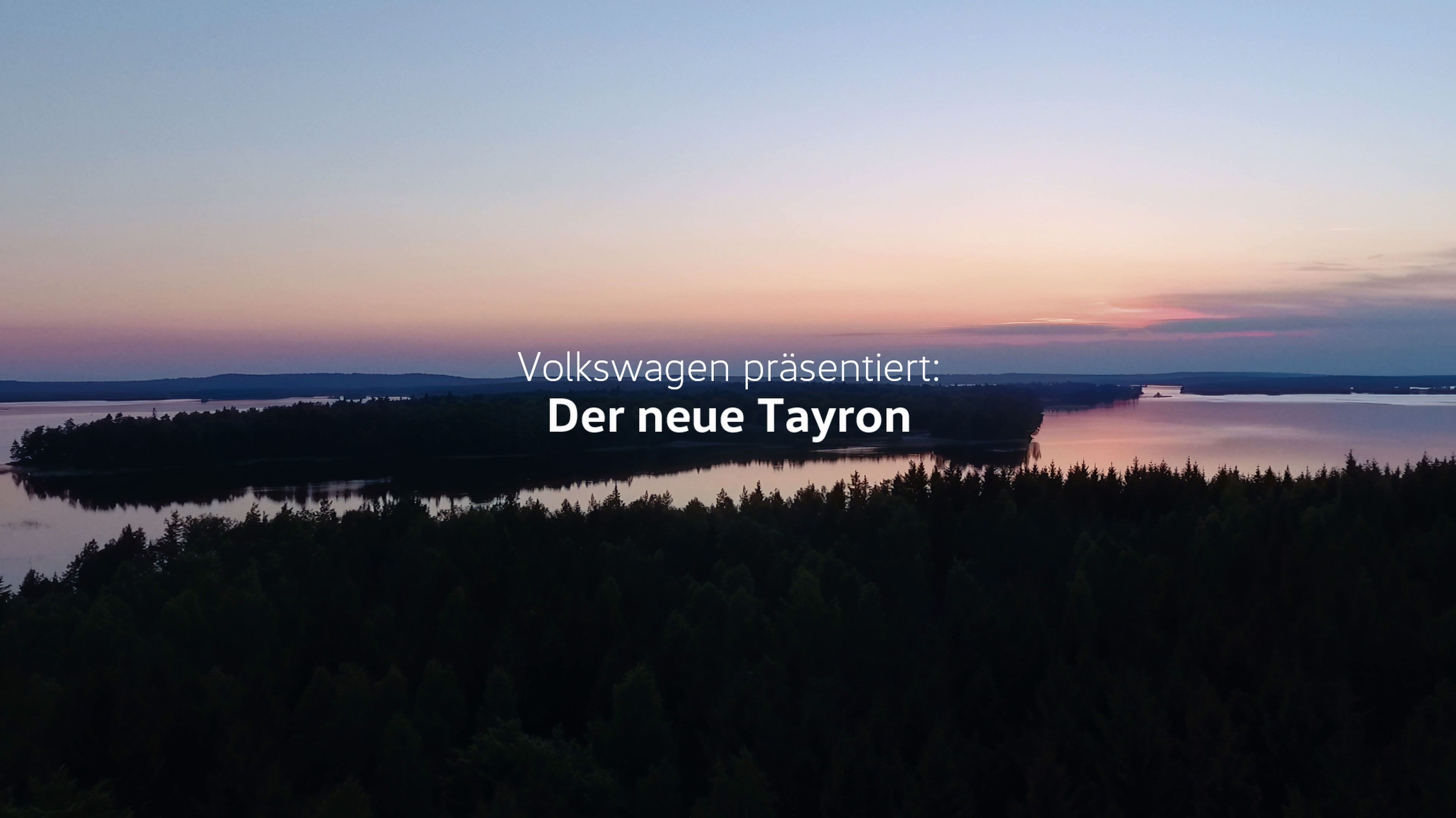 Eine Landschaft mit einem Sonnenuntergang über einem See, umgeben von Wald. Text auf dem Bild lautet: "Volkswagen präsentiert: Der neue Tayron."