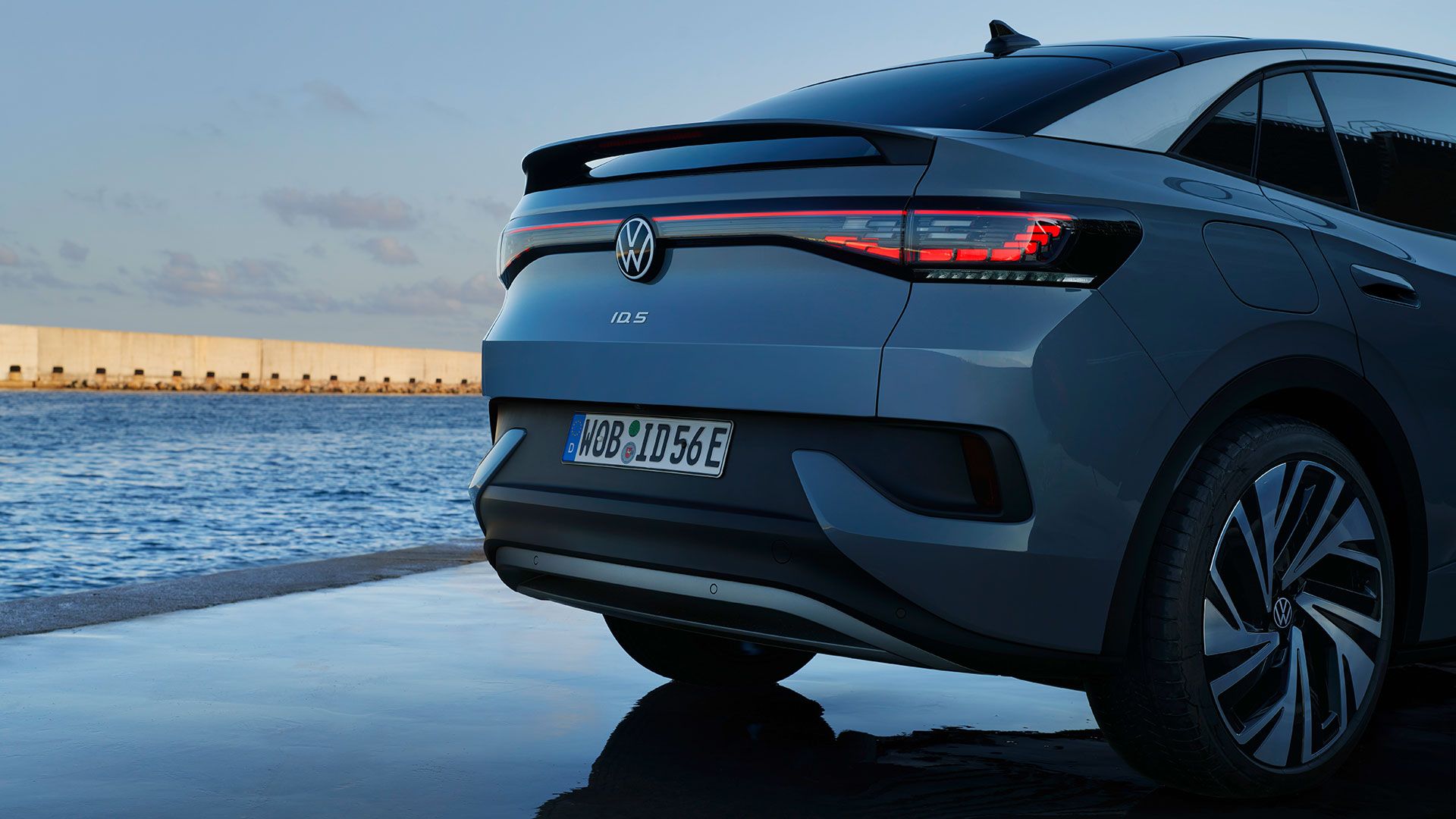 Heck eines stehenden VW ID.5, Abendstimmung am Meer, eingeschaltete LED-Rückleuchten