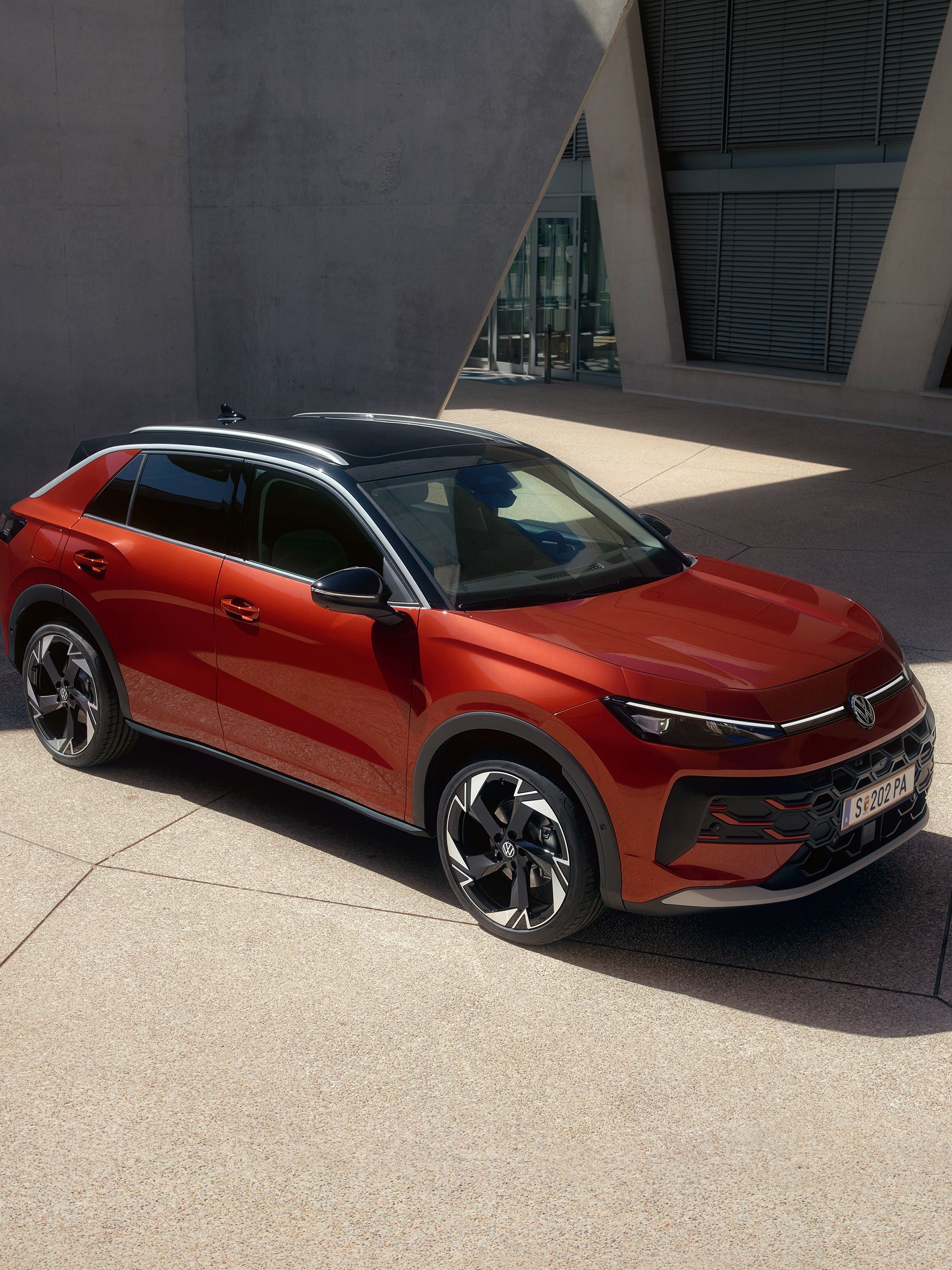 Ein roter VW T-Roc Style steht vor einem modernen Gebäude im Sonnenlicht