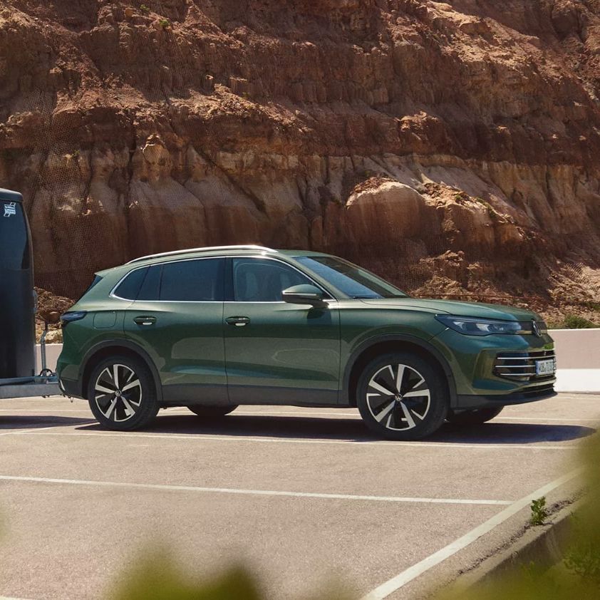 Dunkelgrüner VW Tiguan mit Pferdeanhänger parkt vor einer felsigen Landschaft.