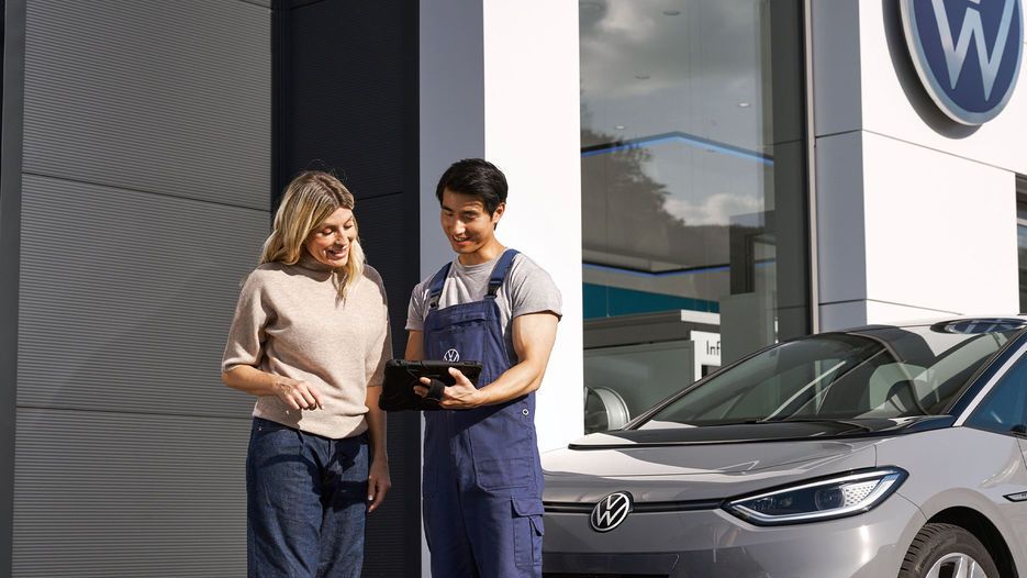 Ein Volkswagen Techniker und eine Kundin stehen vor einem grauen Volkswagen ID.3