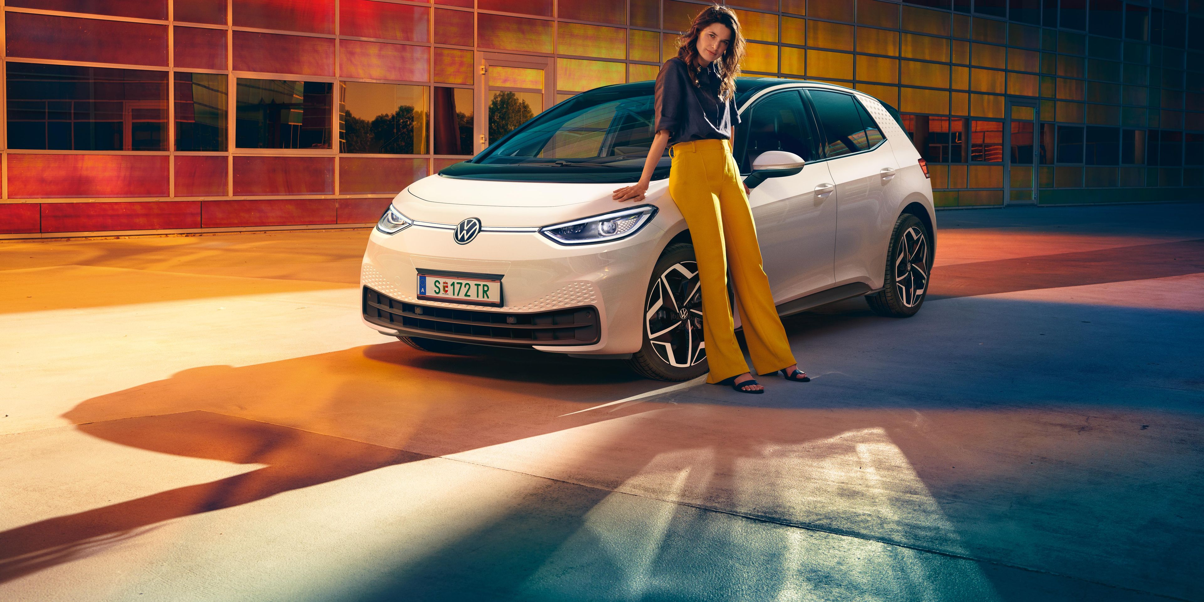 Frau vor dem weißen Volkswagen ID.3, Sicht auf das Fahrzeug von vorne rechts