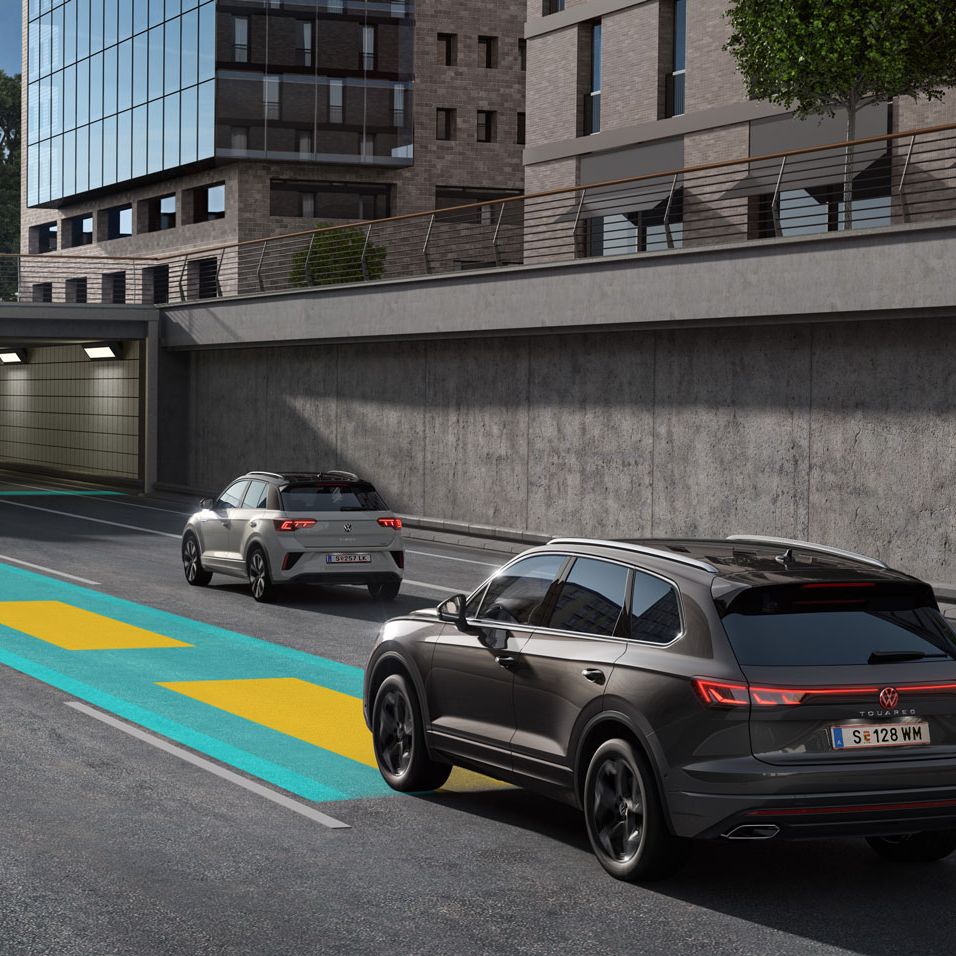 Ein dunkelgrauer VW Touareg fährt auf einer grün-gelben Linie eine Straße entlang auf einen Tunnel zu.