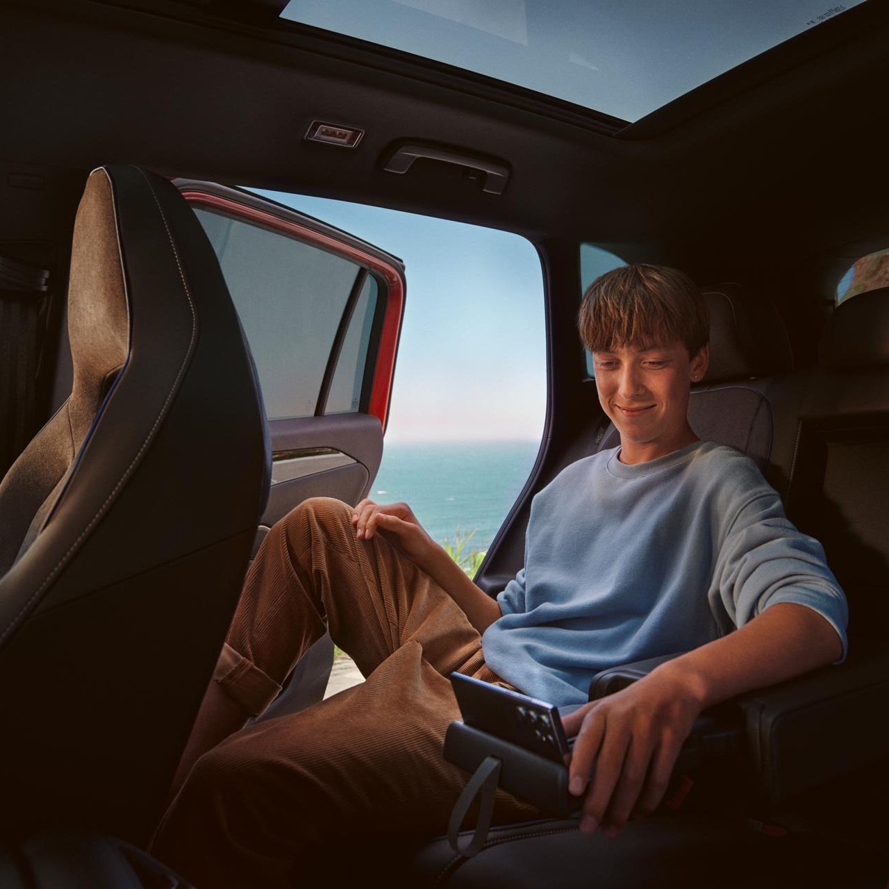 Innenansicht auf die Rückbank des VW Tiguan, wo ein Teenanger auf seinem Tablet, abgestellt auf der Halterung der Mittelkonsole, navigiert. 