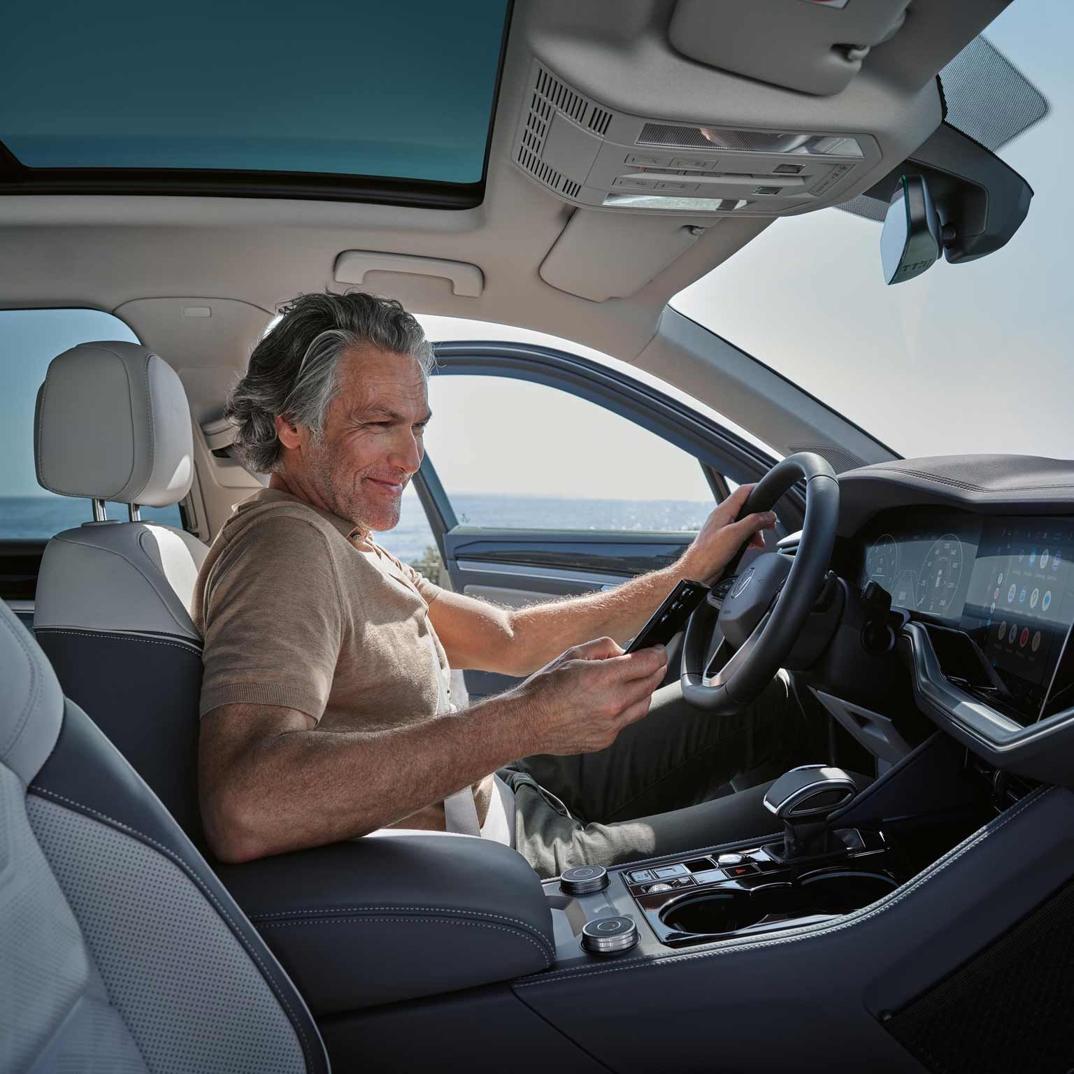 Ein Mann sitzt in einem Volkswagen mit einem Smartphone in der Hand.