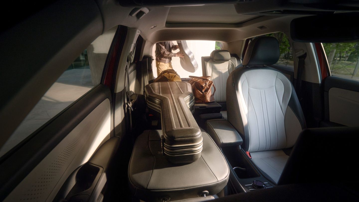 Das Bild zeigt das Innere eines T-Roc mit Ledersitzen. Auf dem Rücksitz liegt ein Gitarrenkoffer. Draußen steht eine Person mit einem weiteren Gitarrenkoffer in der Hand.