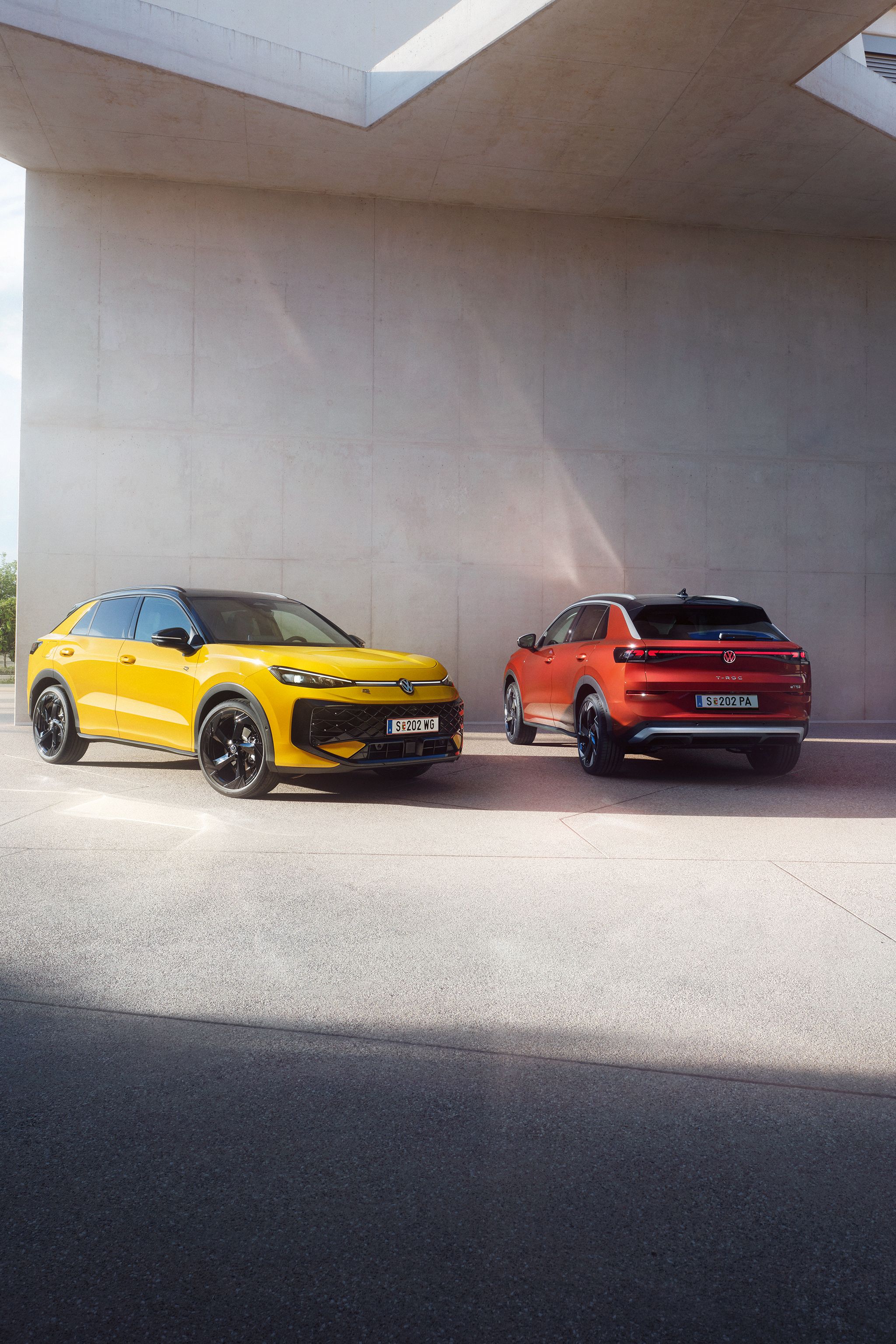 Ein gelber VW T-Roc R-Line und ein roter VW T-Roc Style stehen nebeneinander vor einem modernen Gebäude.