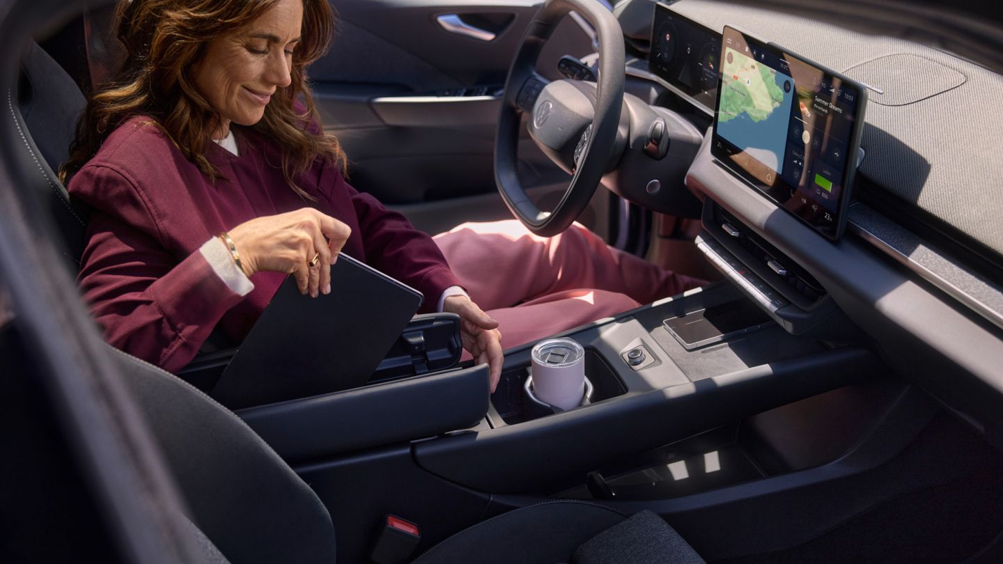 Eine Frau verstaut in einem VW ID.3 Neo ein Tablet in der Mittelkonsole mit Schmetterlingsarmlehne
