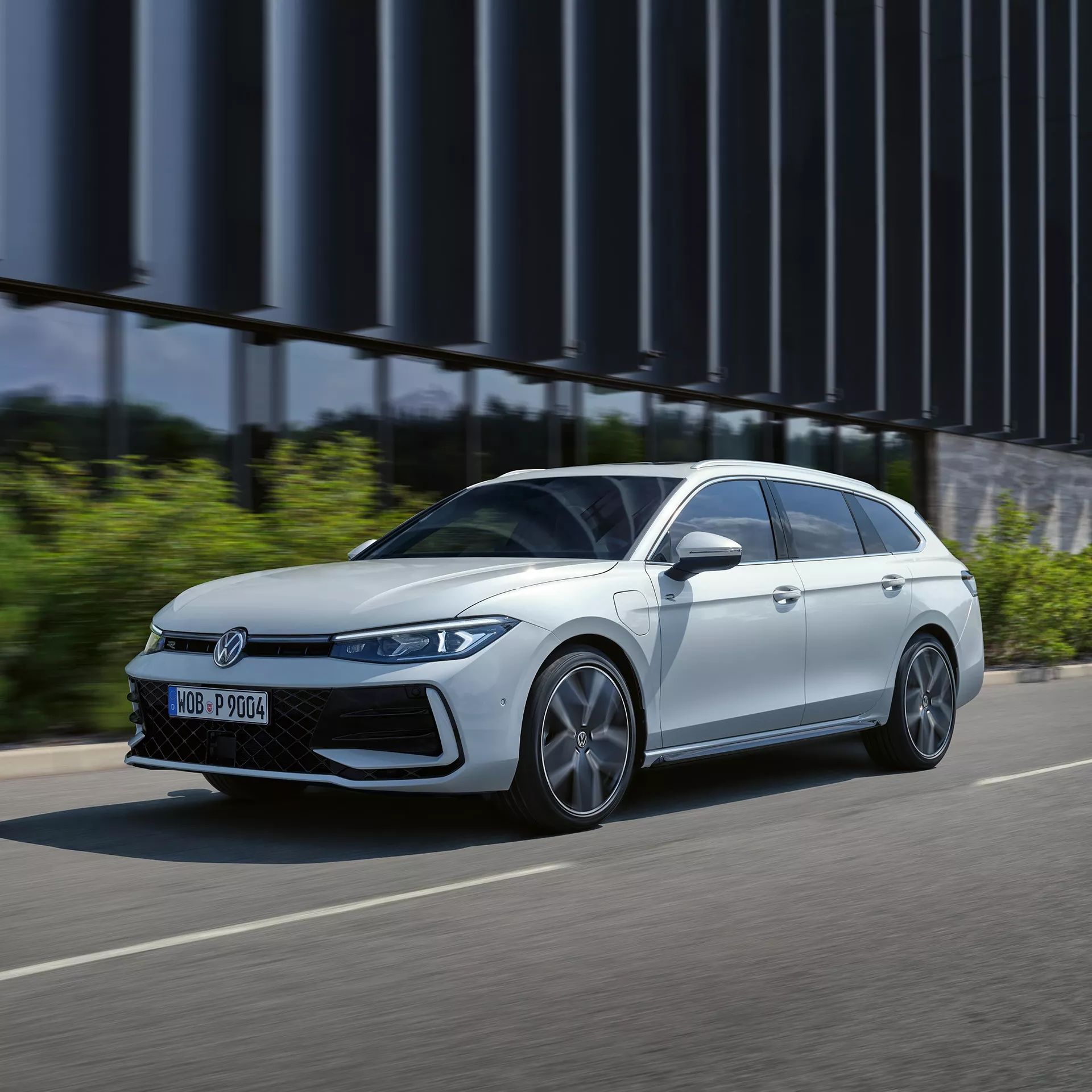VW Passat in weiß fährt seitlich an einem Gebäude vorbei.