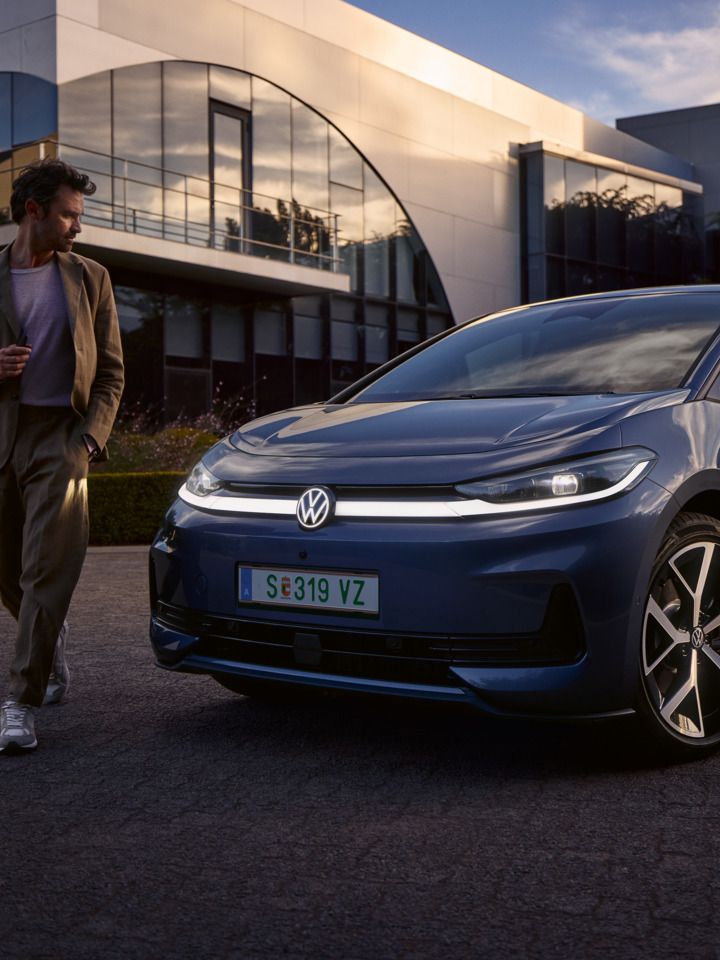 Ein Mann geht um die Front eines blauen VW ID.3 Neo und betrachtet das Lichtdesign