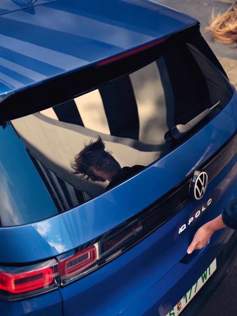 Eine Frau öffnet die Kofferraumklappe eines blauen VW ID. Polo Style.