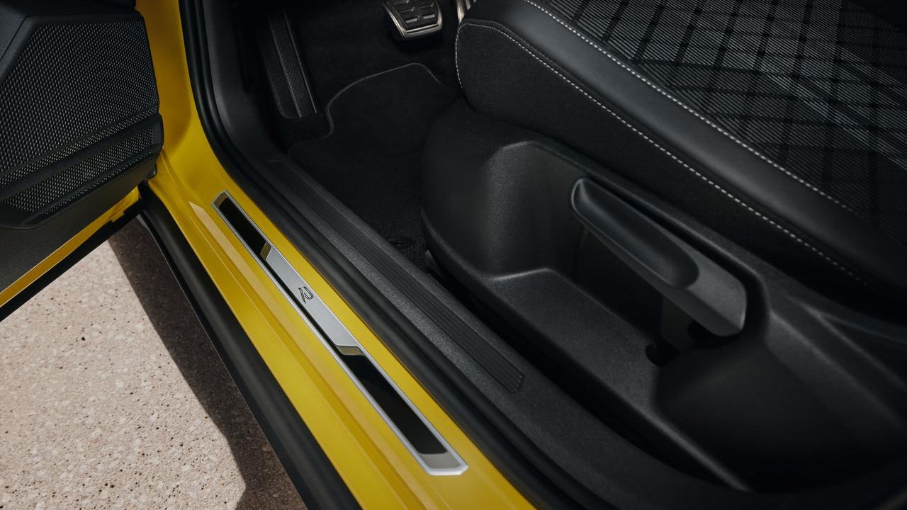 Blick auf unteren Teil des Fahrersitzes des gelben VW T-Cross bei geöffneter Vordertür mit der Einstiegsleiste aus gebürstetem Edelstahl.