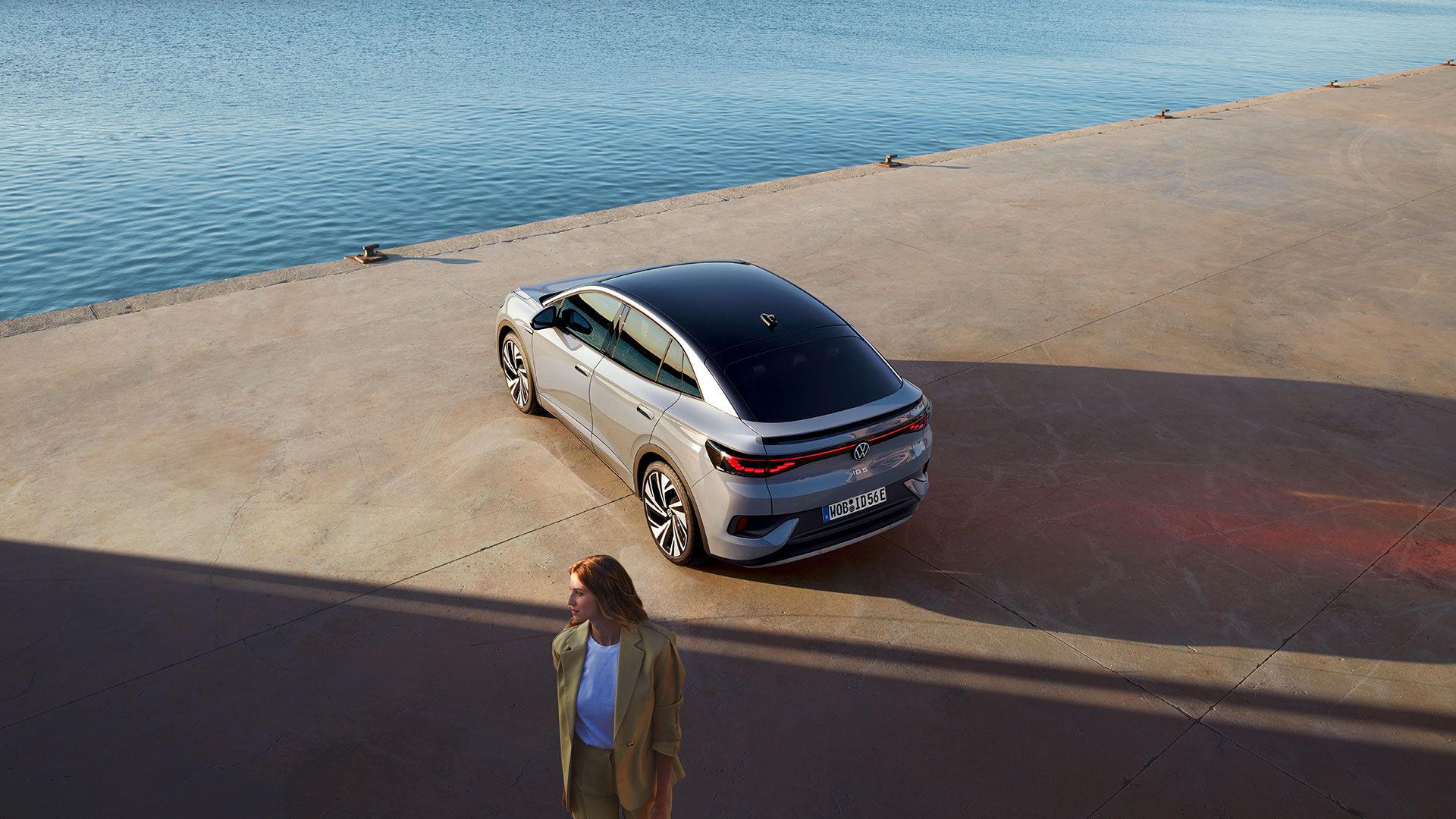 Heckansicht eines VW ID.5 an einem Hafenkai, Blick von schräg oben, im Vordergrund steht eine Frau