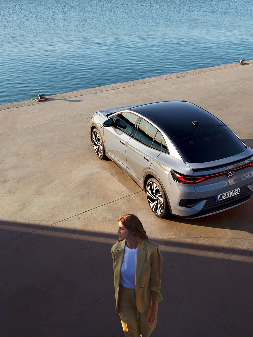 Heckansicht eines VW ID.5 an einem Hafenkai, Blick von schräg oben, im Vordergrund steht eine Frau