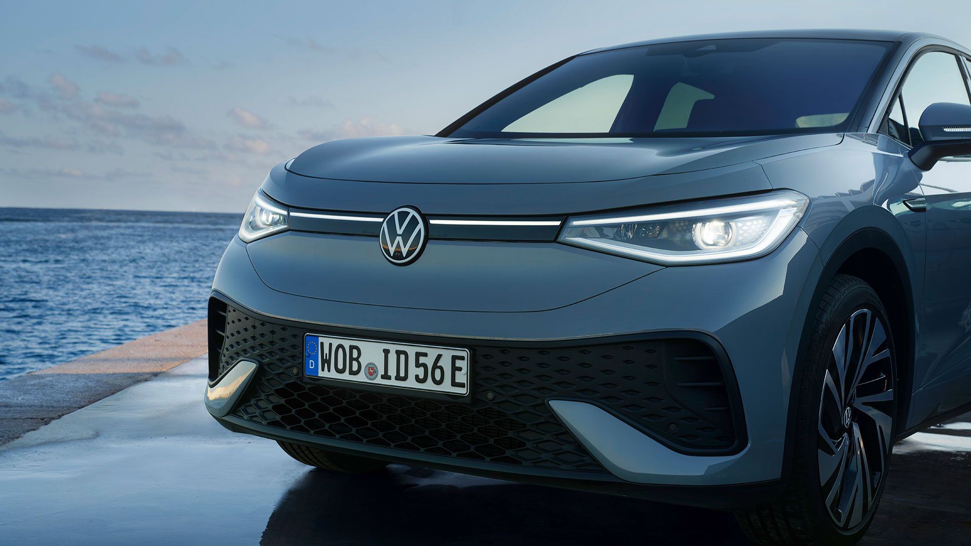 Front eines stehenden VW ID.5 auf einem Hafenkai im Abendlicht, LED-Scheinwerfer eingeschaltet