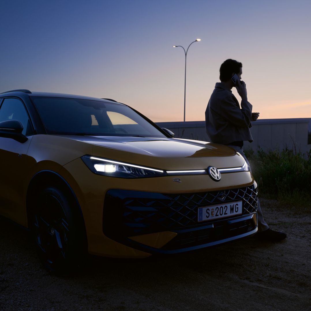 Ein Mann neben einem VW T-Roc R-Line mit eingeschalteten Scheinwerfern und beleuchtetem Logo.