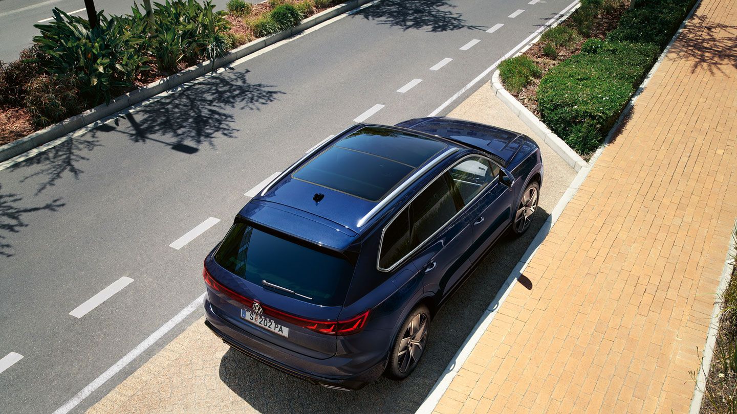Ein VW Touareg R-Line parkt am Straßenrand, Ansicht von schräg oben auf das Heck und Panoramaglasdach.