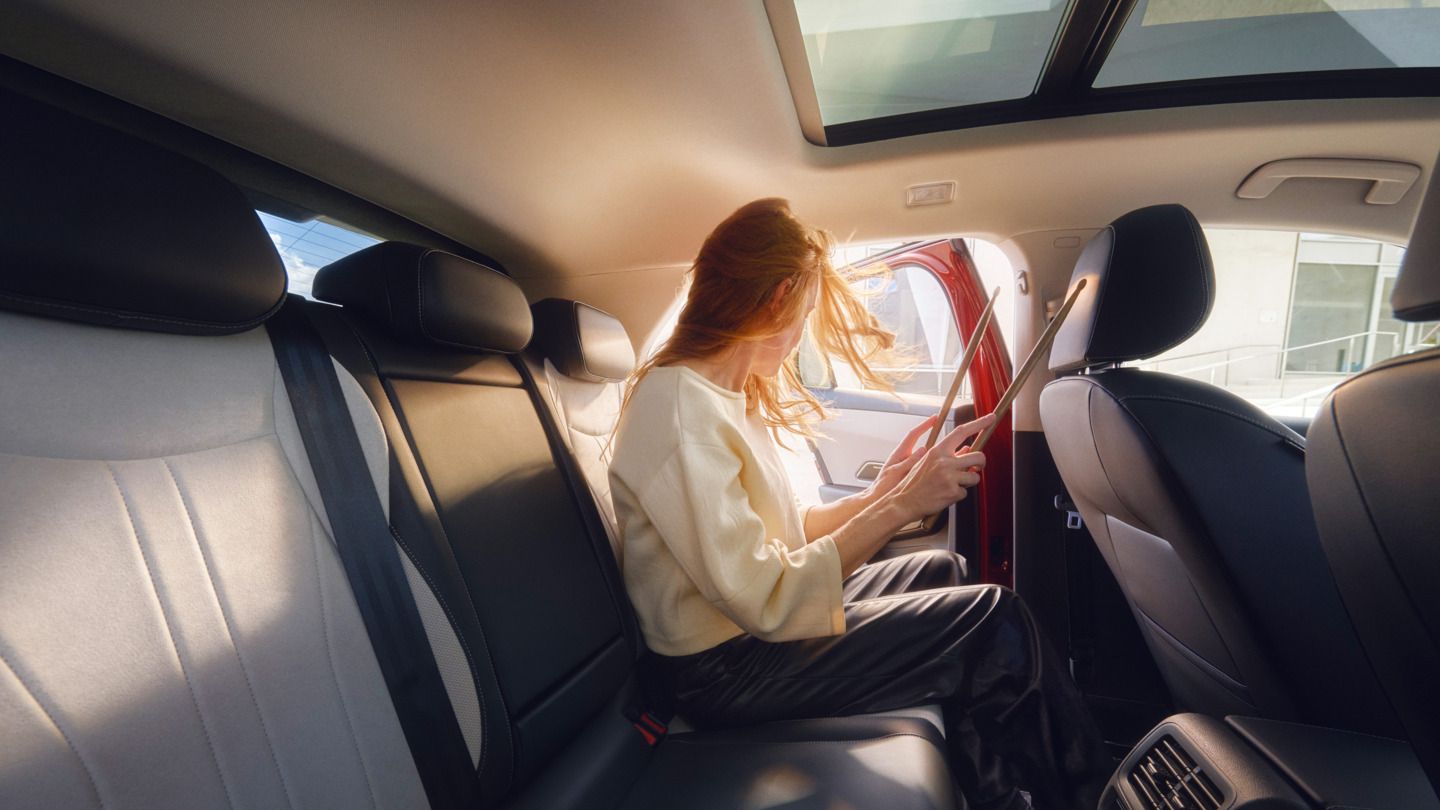 Eine Frau mit langen, roten Haaren sitzt auf der Rückbank eines T-Roc. Sie schaut aus der offenen Tür und hält eine Mappe. Die Innenausstattung des Autos ist modern und komfortabel.
