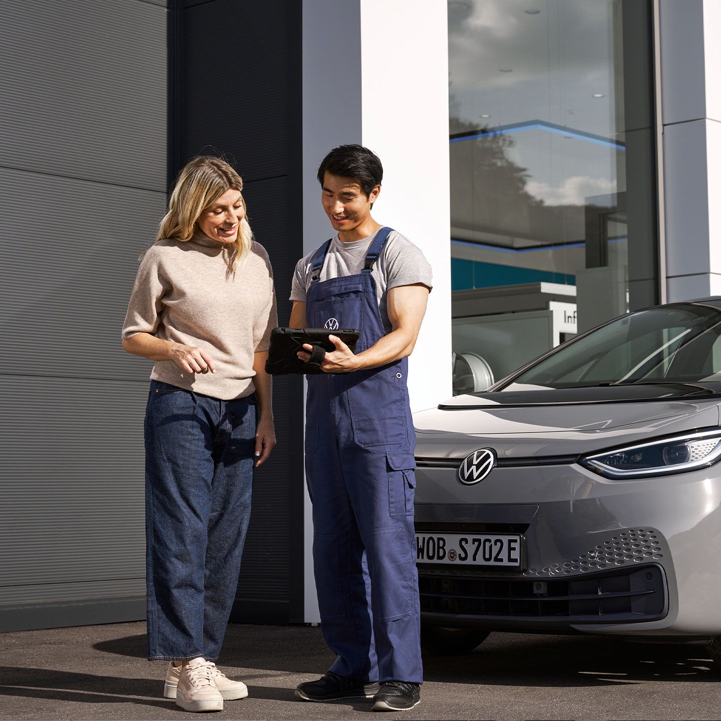 Ein Volkswagen Techniker und eine Kundin stehen vor einem grauen Volkswagen ID.3