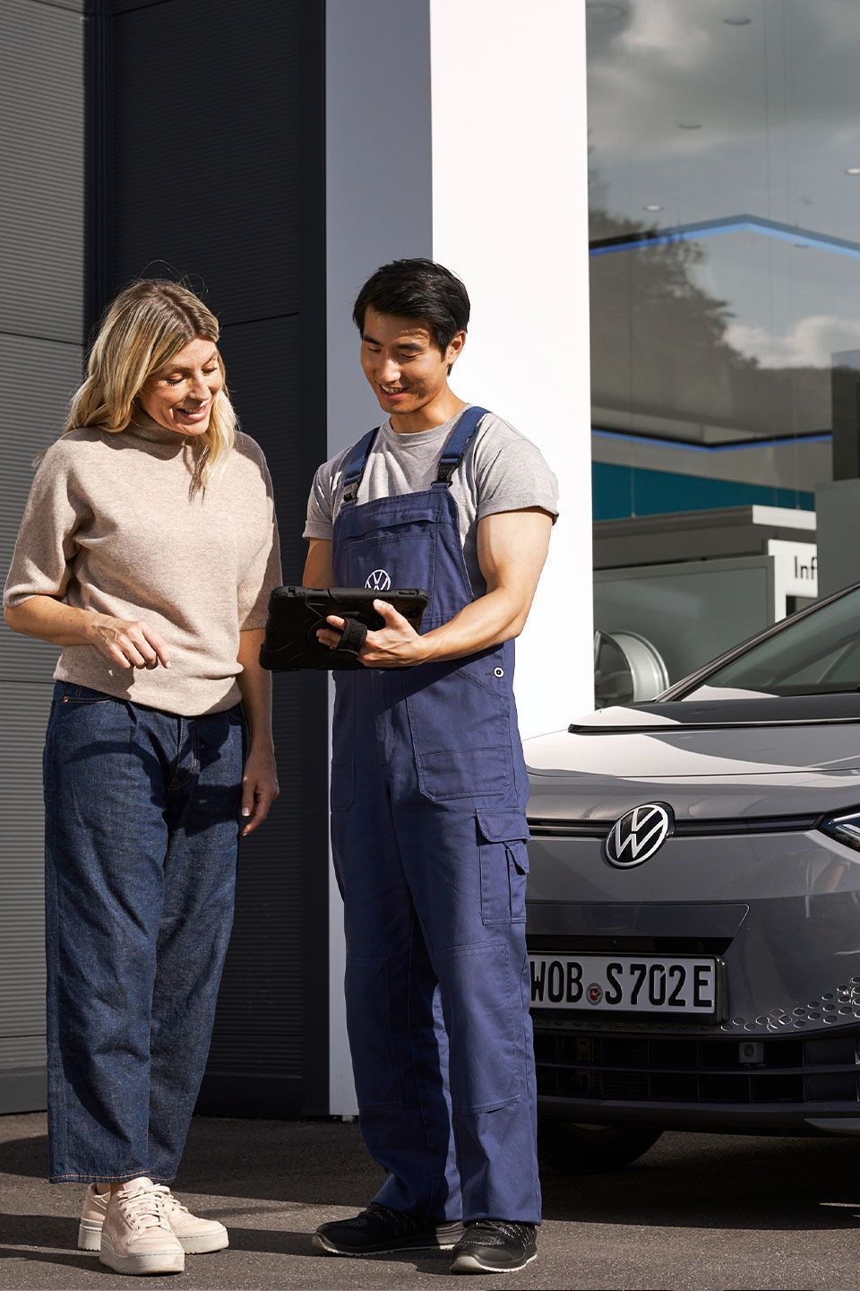 Ein Volkswagen Techniker und eine Kundin stehen vor einem grauen Volkswagen ID.3