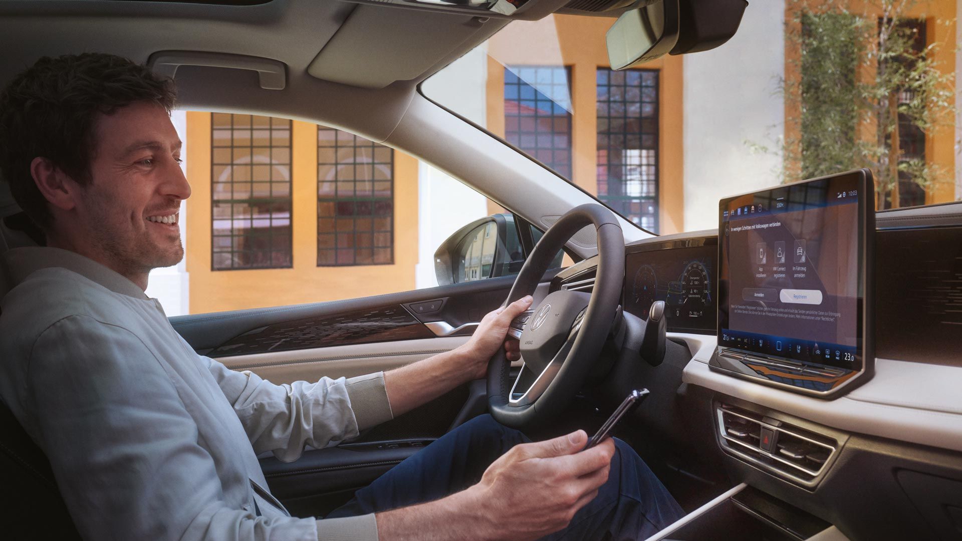 Innenschuss eines VW Tiguan. Ein Mann auf dem Fahrersitz steuert mit seinem Smartphone die optionale VW Connect Plus Anwendung.