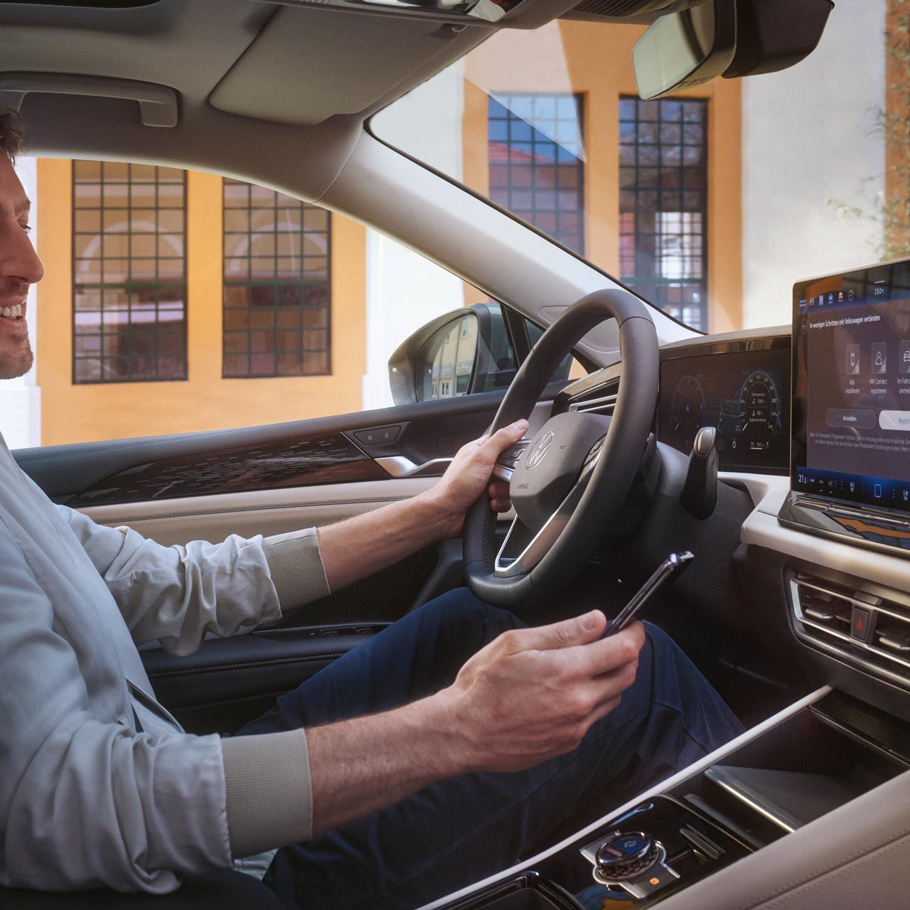 Innenschuss eines VW Tiguan. Ein Mann auf dem Fahrersitz steuert mit seinem Smartphone die optionale VW Connect Plus Anwendung.