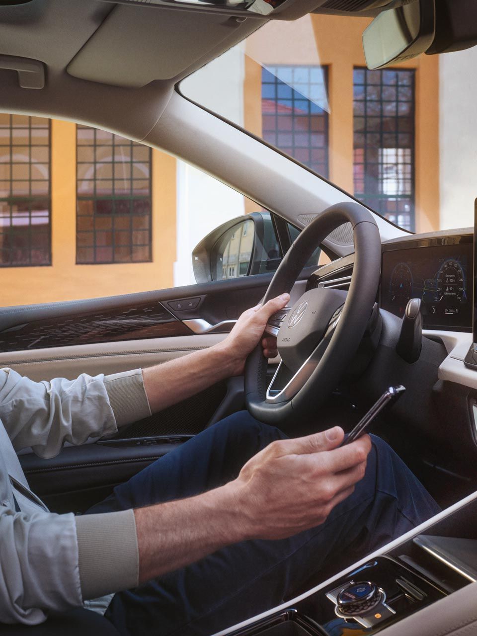 Innenschuss eines VW Tiguan. Ein Mann auf dem Fahrersitz steuert mit seinem Smartphone die optionale VW Connect Plus Anwendung.