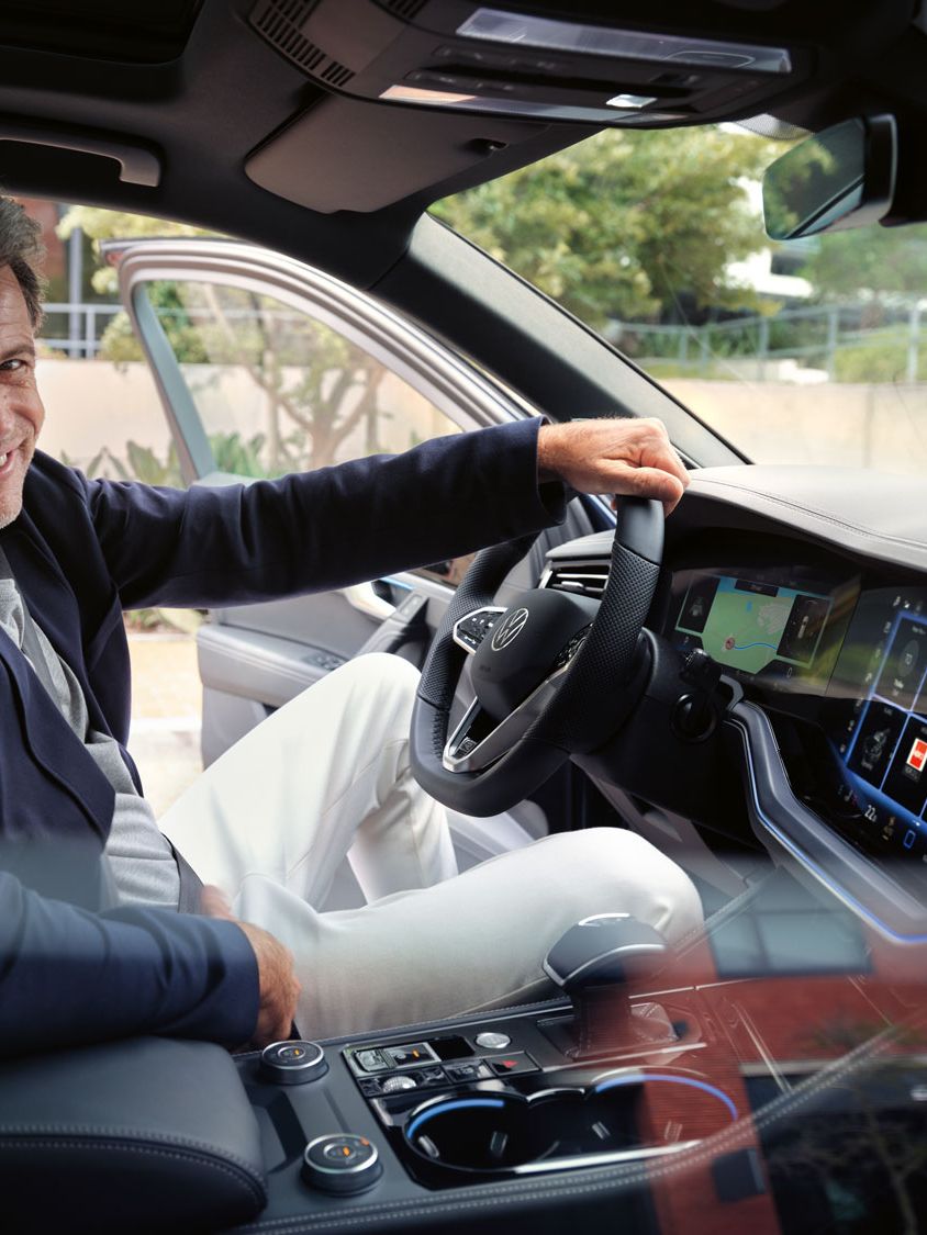 Ein Mann auf dem Vordersitz eines parkenden VW Touareg R-Line blick lächelnd in die Kamera.