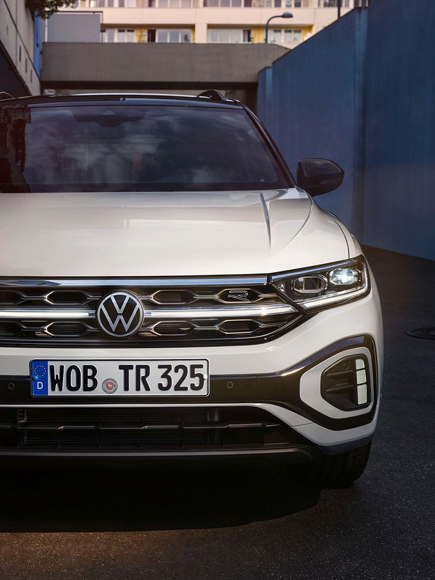 VW T-Roc R-Line Front in Weiß, LED-Tageslichtscheinwerfer und das optionale, illuminierte Kühlerschutzgitter leuchten