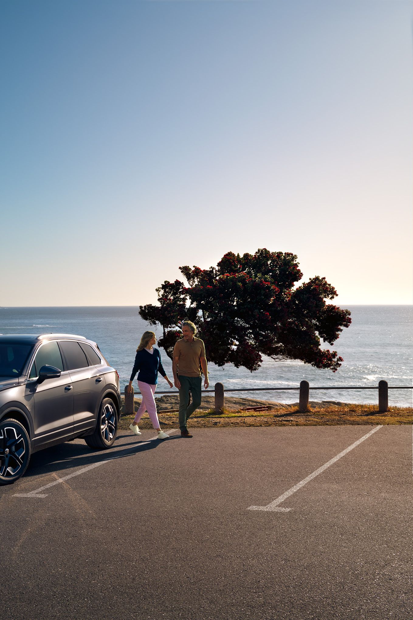 Ein VW Touareg Elegance parkt in der Sonne, Ansicht von schräg vorne, dahinter sind das Meer und die Küste zu sehen.