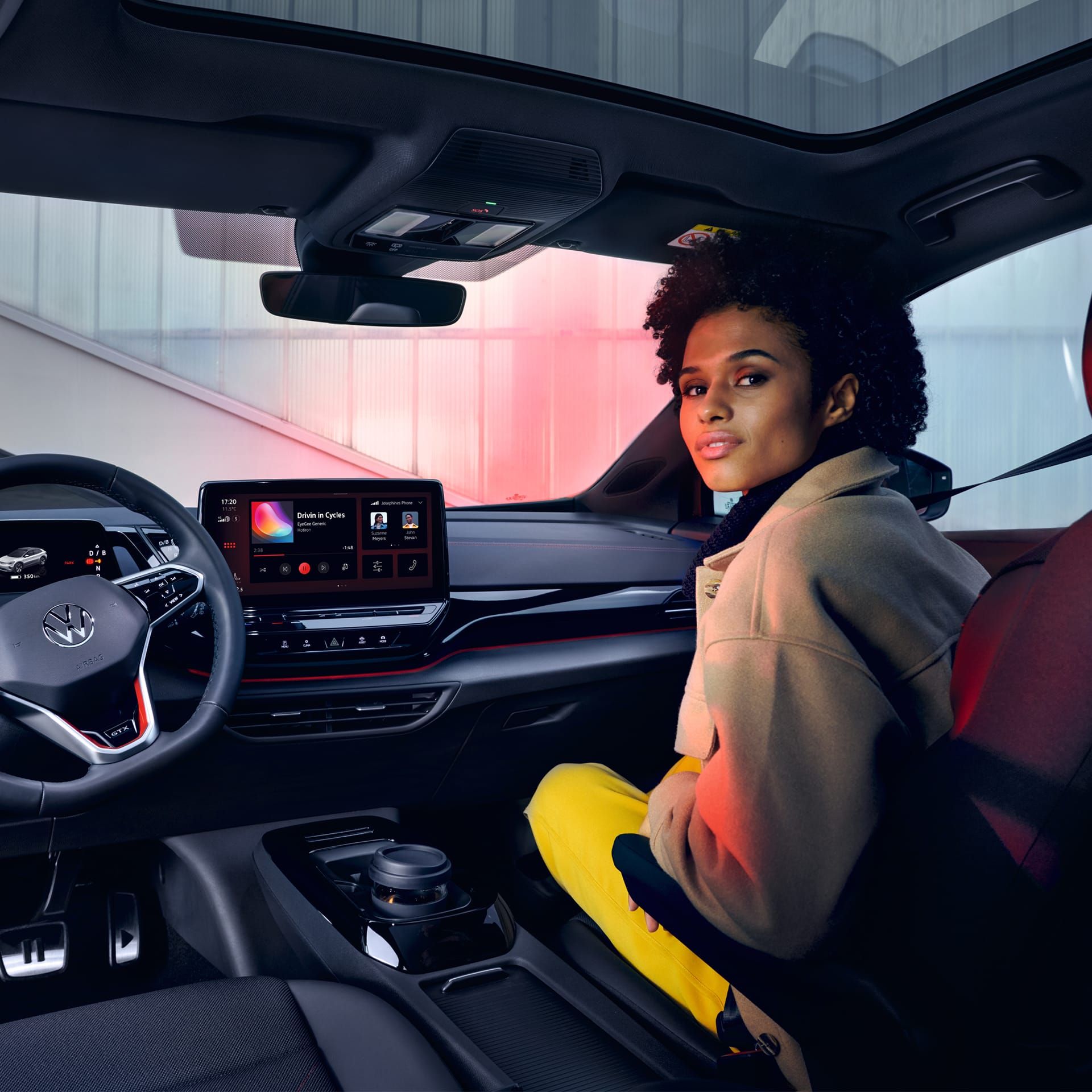 VW ID.4 GTX Innenraum mit Blick auf die Vordersitze und Cockpit. Frau sitzt auf Beifahrersitz mit Blick nach hinten.