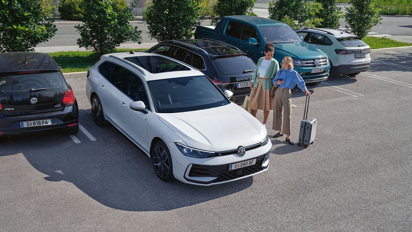Zwei Frauen stehen auf einem Parkplatz neben einem weißen VW Passat, der per 