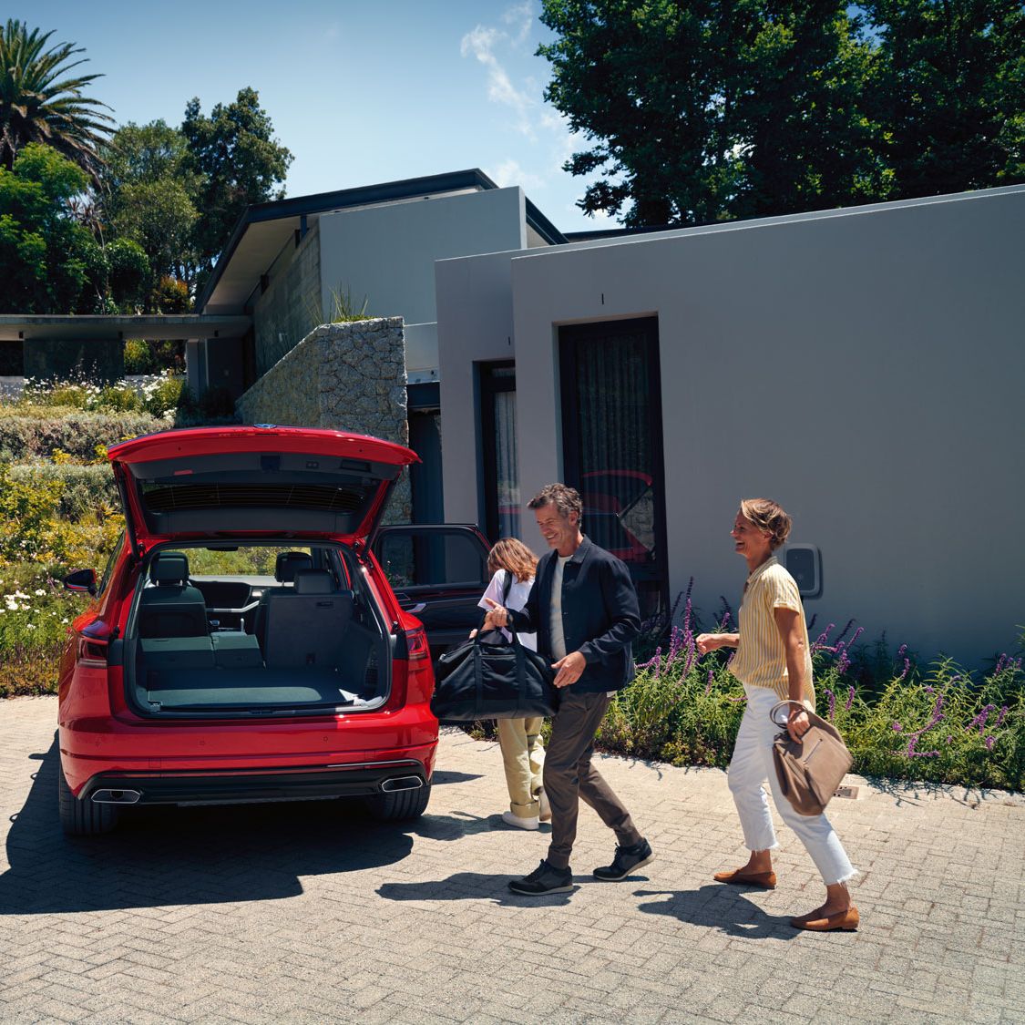 Ein Mann und eine Frau gehen auf einen VW Touareg Elegance eHybrid mit geöffnetem Kofferraum zu.