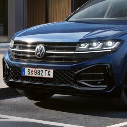 Ein blauer VW Touareg Final Edition steht vor einem Bürogebäude mit Glasfassade - Ansicht von schräg vorne.