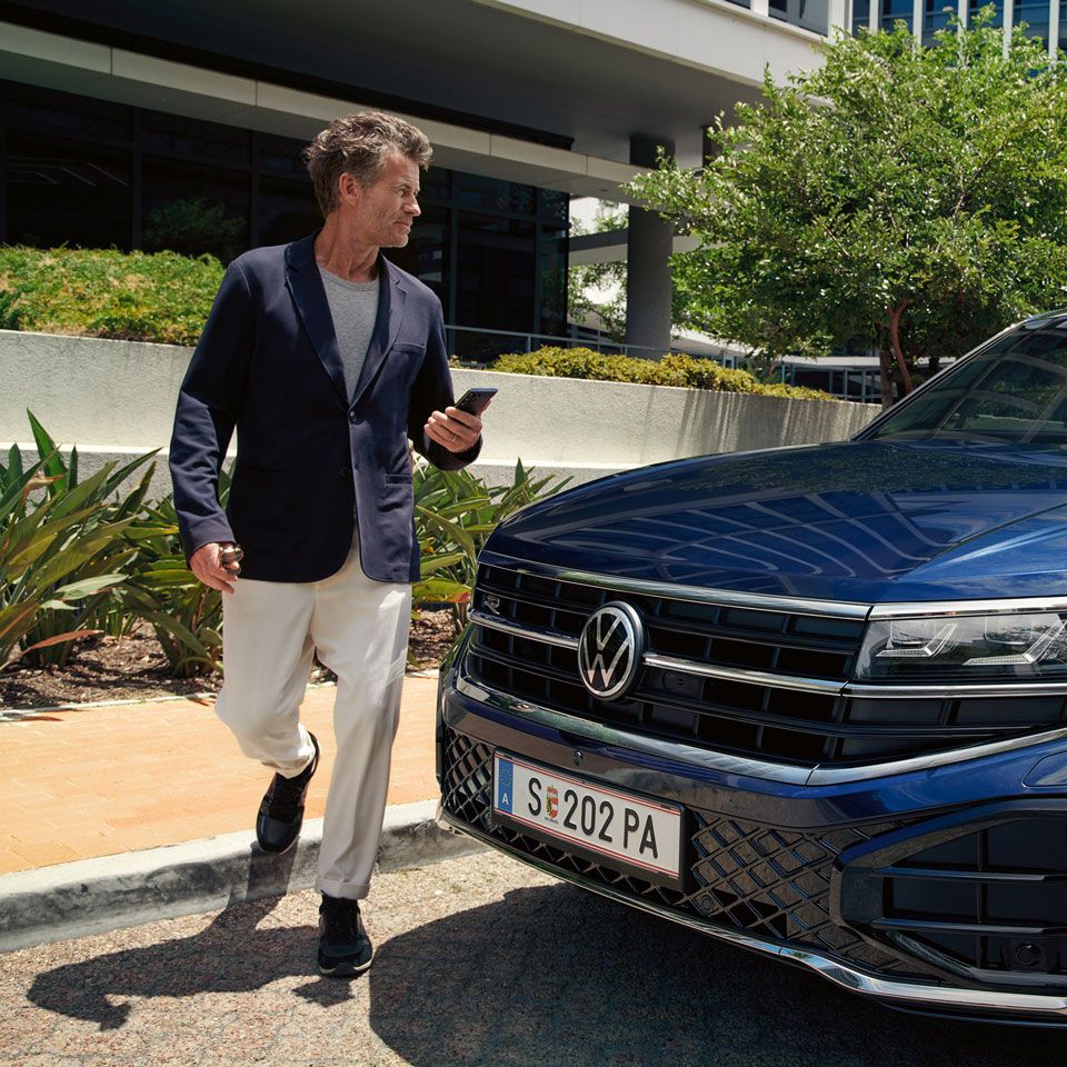 Ein Mann geht an einem parkenden VW Touareg R-Line vorbei.