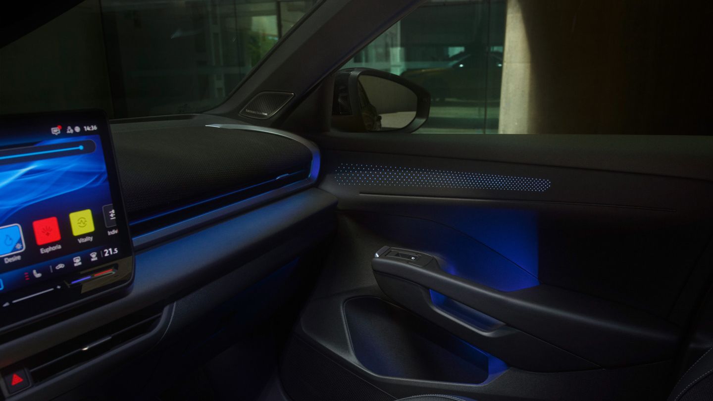 Innenraum eines T-Roc mit einem beleuchteten Touchscreen-Infotainmentsystem, das Navigationsfunktionen, Musik und Wetterinformationen anzeigt. Die Beleuchtung im Innenraum ist blau und schafft eine futuristische Atmosphäre. Das Design ist schlank und minimalistisch.