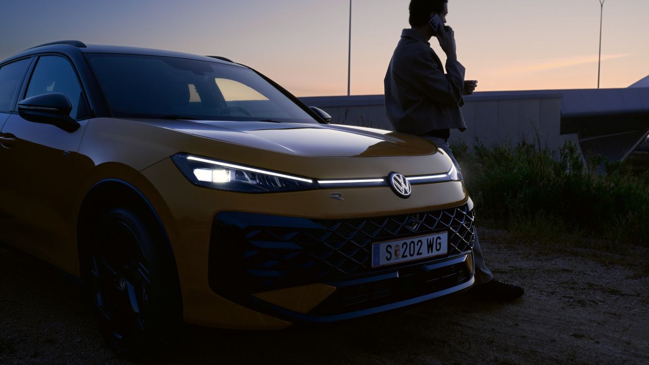 Ein Mann neben einem VW T-Roc R-Line mit eingeschalteten Scheinwerfern und beleuchtetem Logo.