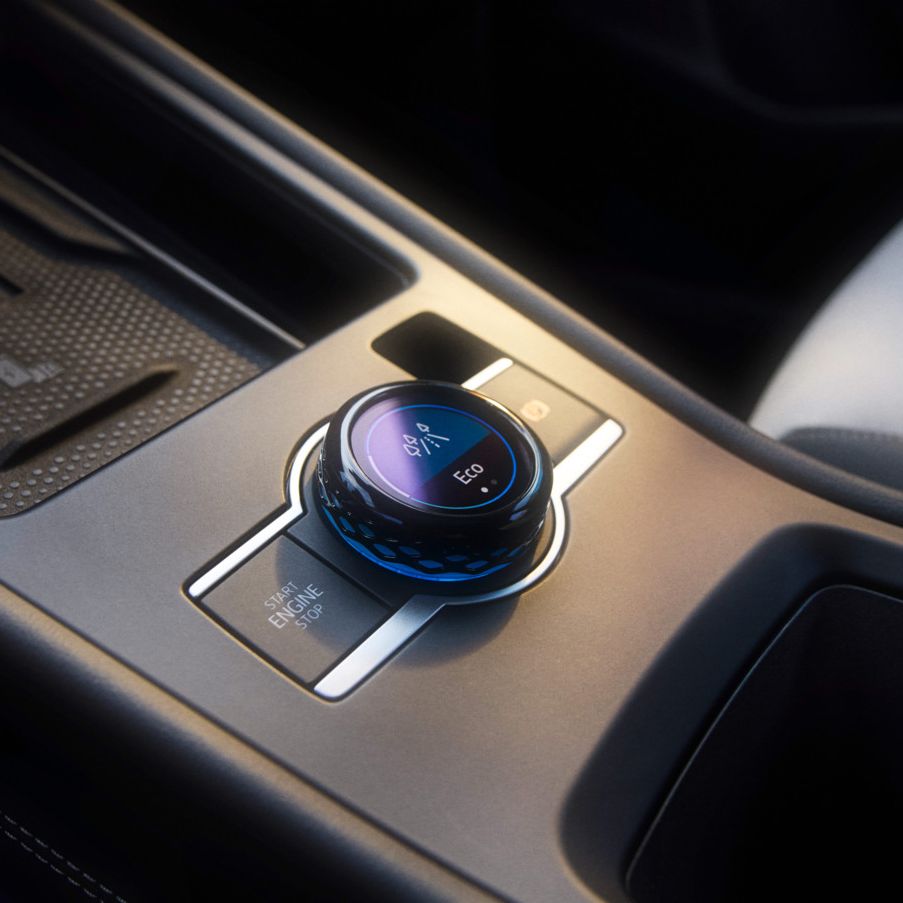 Nahaufnahme einer Mittelkonsole in einem T-Roc mit Fokus auf den Fahrerlebnisschalter. Ein runder Drehknopf mit LED-Anzeigen zur Steuerung verschiedener Fahrzeugfunktionen. Hochwertige Materialien und ein elegantes Design sind zu erkennen.