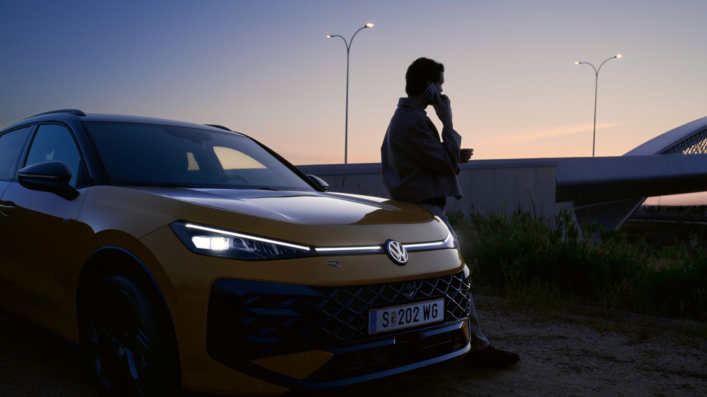 Ein Mann neben einem VW T-Roc R-Line mit eingeschalteten Scheinwerfern und beleuchtetem Logo.