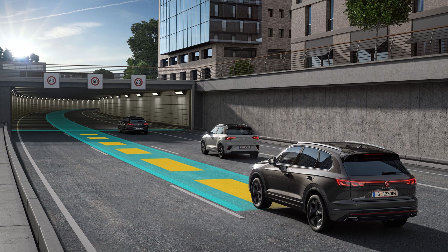 Ein dunkelgrauer VW Touareg fährt auf einer grün-gelben Linie eine Straße entlang auf einen Tunnel zu.