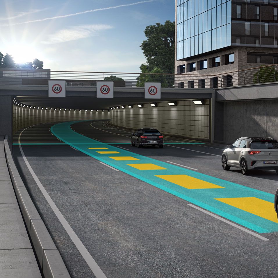 Ein dunkelgrauer VW Touareg fährt auf einer grün-gelben Linie eine Straße entlang auf einen Tunnel zu.