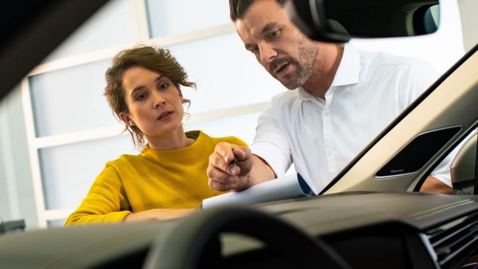 Ein Pärchen ist mit einem VW unterwegs. Er steht beim Kofferaum. Sie im Vordergrund und schaut in die Kamera.