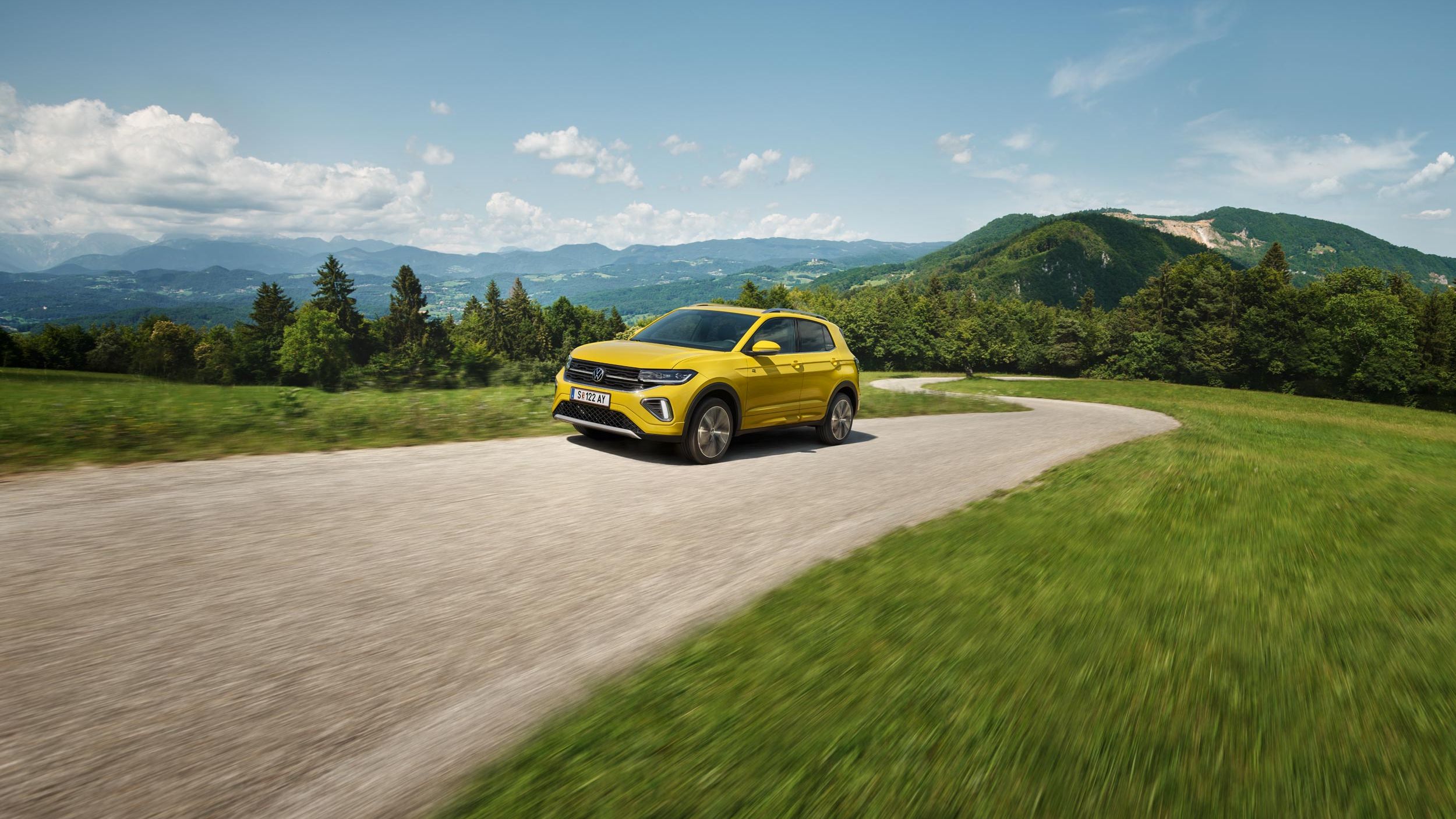 Ein gelber VW T-Cross auf einer Straße in hügeliger Landschaft.
