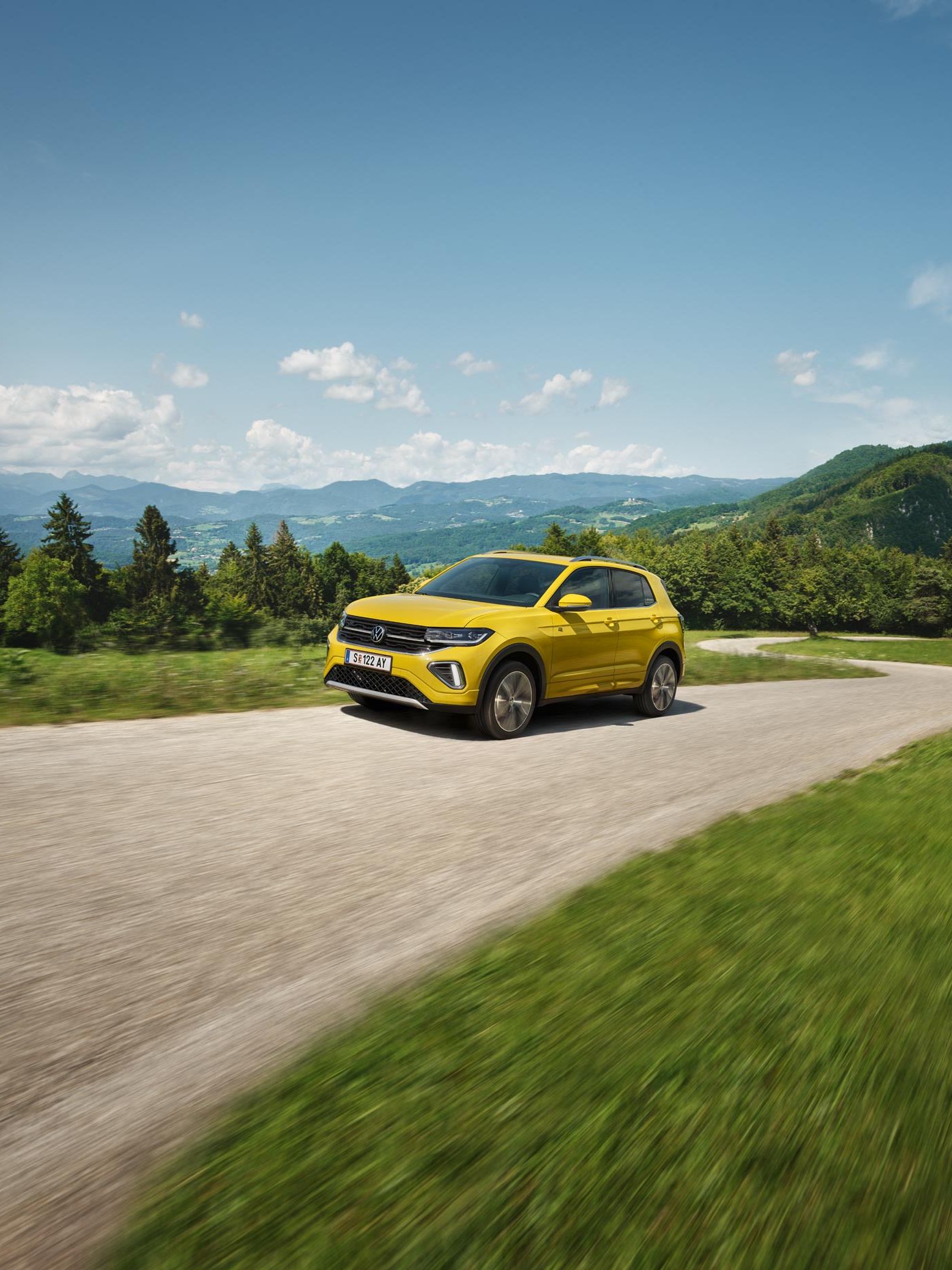 Ein gelber VW T-Cross auf einer Straße in hügeliger Landschaft.